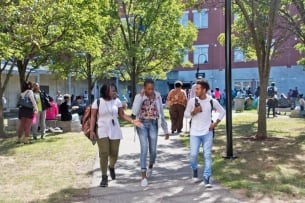 Three students walk in the tree-lined courtyard at Roxbury Community College. 
