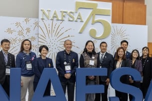 A group of people stands in front of a sign that says "NAFSA 75"