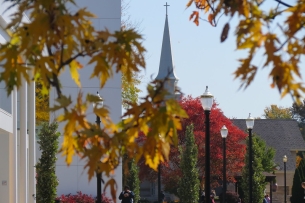 Students walk on Walsh University's campus in the fall with a steeple topped with a cross in the background.