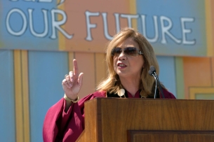 Mildred García speaking at her inauguration at Cal State Dominguez Hills. She is wearing academic regalia and sunglasses.