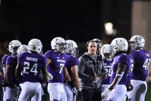 Northwestern Wildcats football coach Pat Fitzgerald surrounded by players in helmets and purple and white uniforms.