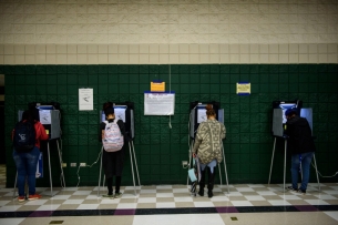 Four voters stand in their polling booths against a green background.