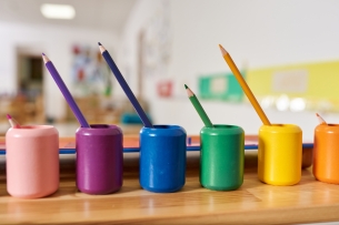 6 colorful Montessori pencil holders in foreground of blurred classroom (opinion)