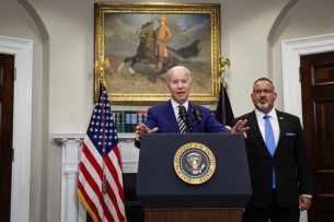 President Biden stands at a podium next to Education Secretary Miguel Cardona