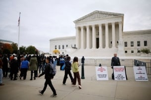 The scene in front of the Supreme Court Oct. 31, when the court heard arguments in two cases challenging race-conscious admissions in higher education: a lone opponent of affirmative action, with protest signs, stands next to a group of mostly young people rallying in support of affirmative action.