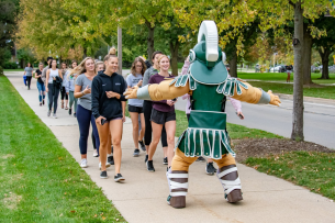 Students walk on Michigan State University's campus for the annual Exercise Is Medicine on Campus Health Homecoming Walk with the Spartan mascot in front
