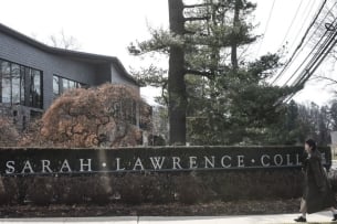 A sign for Sarah Lawrence College, as person in a jacket walks past.