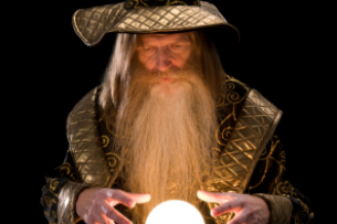 A wizard, dressed in a robe and pointy hat, stands with his hands hovering above a glowing crystal ball.