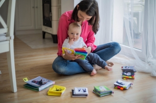 A mother holds her baby while playing with toys