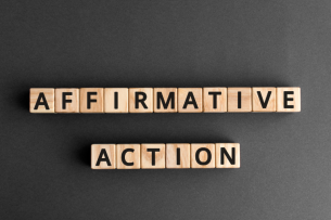 Wooden blocks spelling out the words "AFFIRMATIVE ACTION" against a plain dark background.