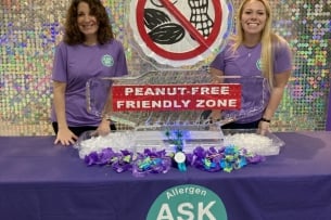 Two Duke Dining staff members smile at a table featuring a peanut-free friendly zone ice sculpture to share the launch of the Ask Me program. 