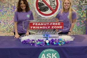Two Duke Dining staff members smile at a table featuring a peanut-free friendly zone ice sculpture to share the launch of the Ask Me program.