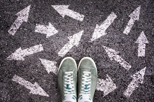 Shot of feet in sneakers with white arrows pointing in all different directions on the ground around them.