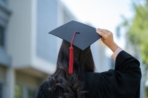 A woman stands with her back to the camera holding her graduation cap.  