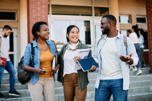 Three multicultural students walking with books in their arms and happily talking together