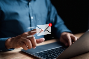 Concept image of a man's hand touching an email icon floating over his laptop keyboard.