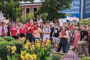 A student wearing a red shirt and a red bandanna uses a megaphone to address a crowd of other protesters outside West Virginia University's Mountainlair student union.