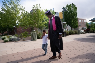 Male African American college graduate walking with his 3-year-old son on graduation day at a university