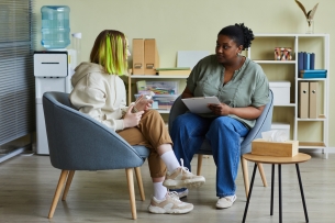 A staff member talks with a female student, sitting in chairs in an office.