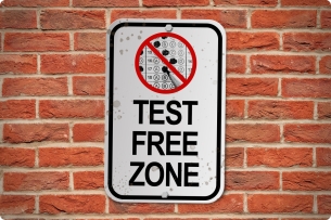 A sign (approximating a road sign) reads "Test Free Zone," with a standardized test score sheet circled and crossed through in red.