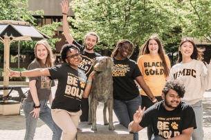 A group of happy-looking students wearing black and yellow-gold swag and gear pose on the University of Maryland Baltimore County campus, presumably for orientation.