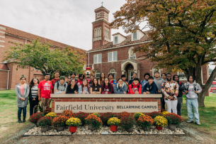 A group of students stands behind a sign reading "Fairfield University Bellarmine Campus"