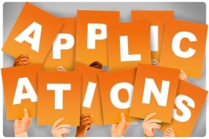 Hands holding up orange signs that together spell out the word "applications"