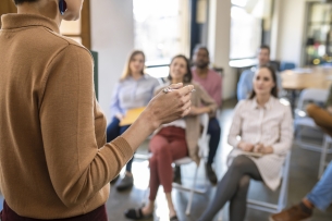 Back view of a woman lecturer giving presentation to a group of businesspeople.