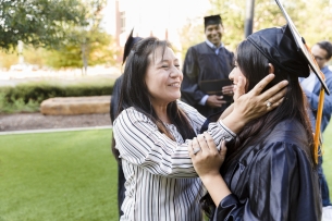 Proud mother holds her young adult daughter's head in her hands on her daughter's graduation day.