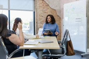 Three women talk at a business presentation in a conference room.