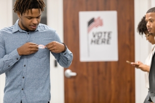 After voting, the young adult man proudly sticks an "I voted" sticker to his shirt.