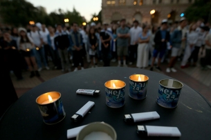 A photo of small candles and lighters, which say "USC Hillel," with a group of people in the background.