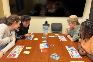 Four students play a board game on a brown table
