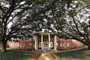 A columned brick campus hall surrounded by trees