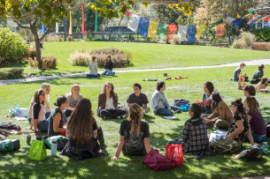 A group of students sits on the lawn at Naropa University on a sunny day