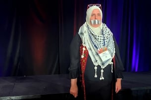 A photograph of Ahlam Muhtaseb, professor of communication studies at California State University, San Bernardino, standing with duct tape on her mouth. Her head is covered and she wears a kaffiyeh around her neck.