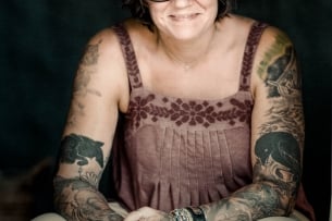 A woman in glasses with tattoos sits for a portrait