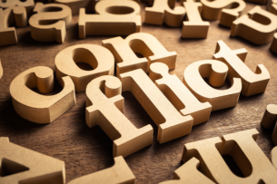 The word "conflict" spelled out in wooden blocks, with other wooden alphabet blocks strewed around.