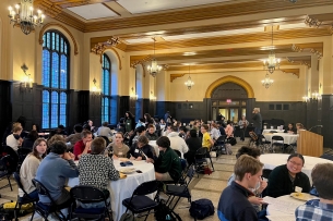 Sophomore students at Carleton College attend a banquet dinner, sitting at round tables with white tablecloths in a large meeting space.