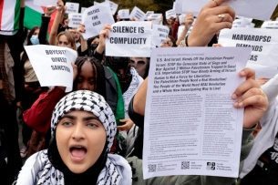 Harvard students hold up white pieces of paper with black text calling for "Justice for Gaza" as part of a pro-Palestinian protest