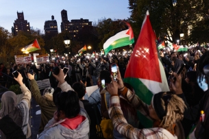 A photo of a student rally at nighttime, with multiple Palestinian flags flying.