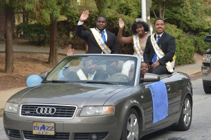 A group of Spelman, Morehouse and Clark Atlanta students stand in the back seat of a car waving, wearing formal suits, dresses and sashes for homecoming.
