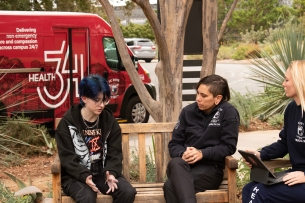 A student talks to two professionals with the University of California, Davis, Fire Department on a bench in front of a red van