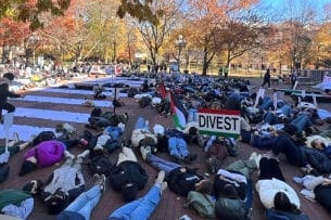 University of Michigan students protest for divestment, lying on the group and holding up a sign in the colors of the Palestinian flag that says, "Divest."