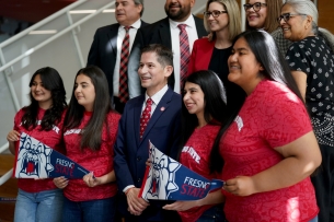 A man in a suit and tie flaked by four girls in red T-shirts