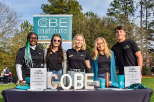 Five Coastal Carolina students stand behind a table during the spring 2024 organizational kickoff day event.