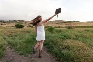 A teen girl wears a white dress, western boots and a graduation cap