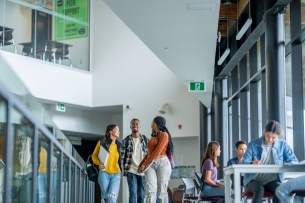 Three students walk to class wearing backpacks and holding books