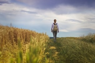 A student wearing a backpack walks in a field.