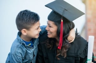 A mother in graduation regalia smiles at her son.